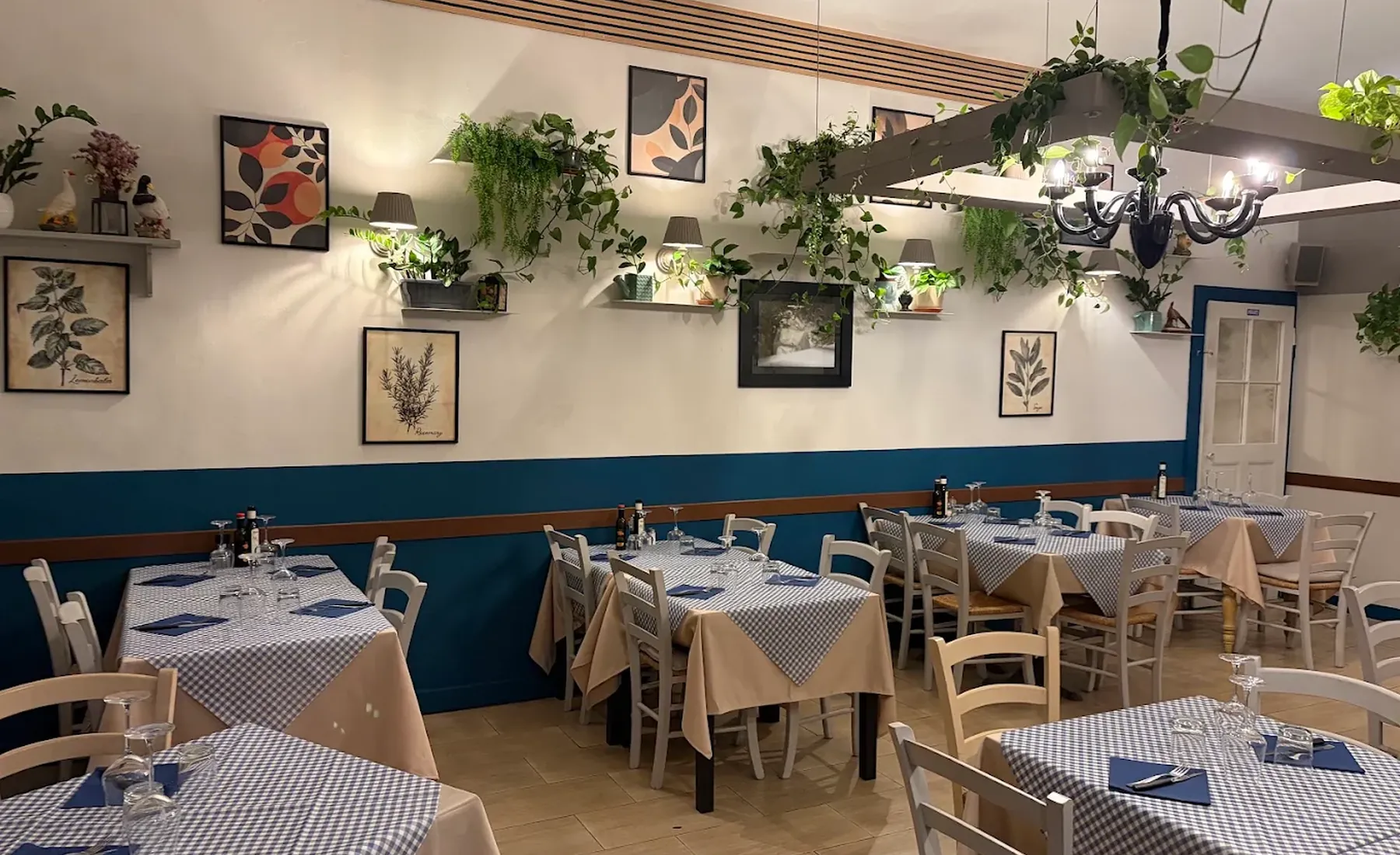 La sala del ristorante Da Noi Due a Cecina: tavoli con tovaglie a quadretti blu, sedie bianche di paglia e piante alle pareti
