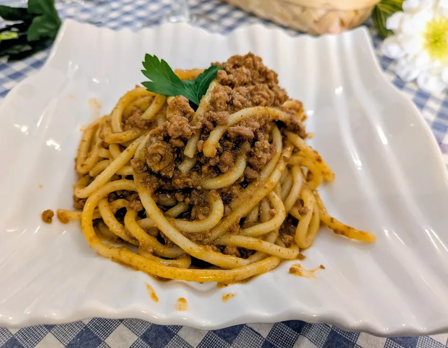 Pici al ragù di manzo serviti su piatto bianco con tovaglia a quadretti