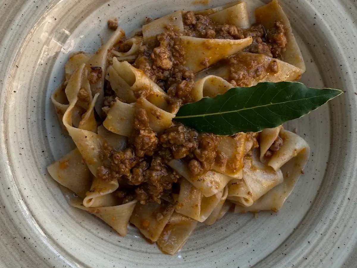 Pappardelle al ragù di cervo servite in un piatto di ceramica con foglia di alloro